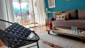 A living room with a sofa, a chair, a coffee table, and a view through a glass door to an outdoor area.