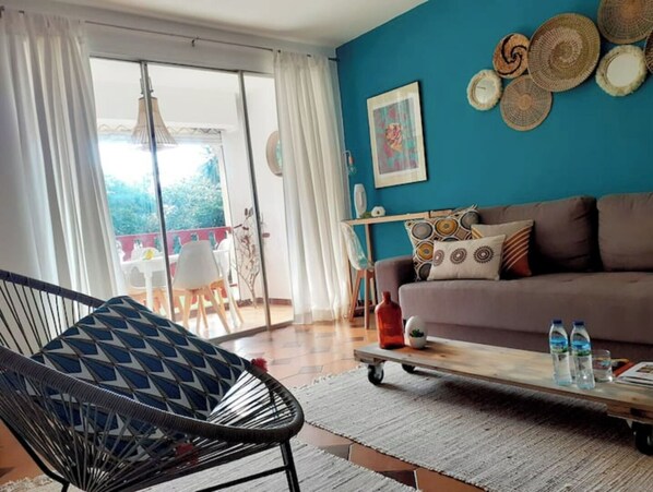 A living room with a sofa, a chair, a coffee table, and a view through a glass door to an outdoor area.