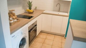 A compact kitchen with a washing machine, a sink, and a countertop with a fruit bowl.