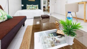 A modern living room with a brown sofa, a glass coffee table with a magazine, a small potted plant, and a water bottle. - Housing 3mn from the sea! 🌴🌊 Sea view, private beach and pool access (Schoelcher)