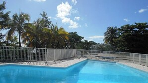 A clear blue pool surrounded by a white fence, with palm trees and a clear sky in the background. - Housing 3mn from the sea! 🌴🌊 Sea view, private beach and pool access (Schoelcher)