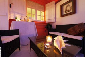 A cozy room with a dining table, a sofa, and a chair. There is a candle on the table and a framed picture on the wall.