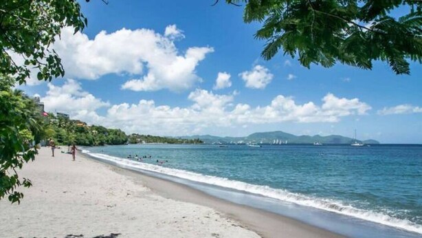 Ein Strand mit blauem Himmel, ruhiger See und Bergen in der Ferne.