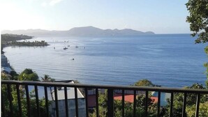 Ein Balkon mit Tisch und Stühlen, mit Blick auf ein ruhiges Meer mit Booten und weiter Küste.