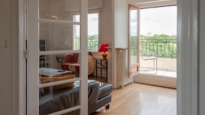 Une chambre dotée d’une porte-fenêtre coulissante donnant sur un balcon, d’un lit avec une tête de lit, d’une petite table avec une lampe et d’une vue sur la verdure environnante.