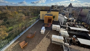 Une terrasse sur le toit offrant une vue sur la ville, un petit bâtiment jaune et un banc en bois.