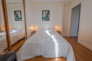Une chambre d’hôtel avec un grand lit, deux tables de chevet, un miroir et des œuvres d’art accrochées aux murs.