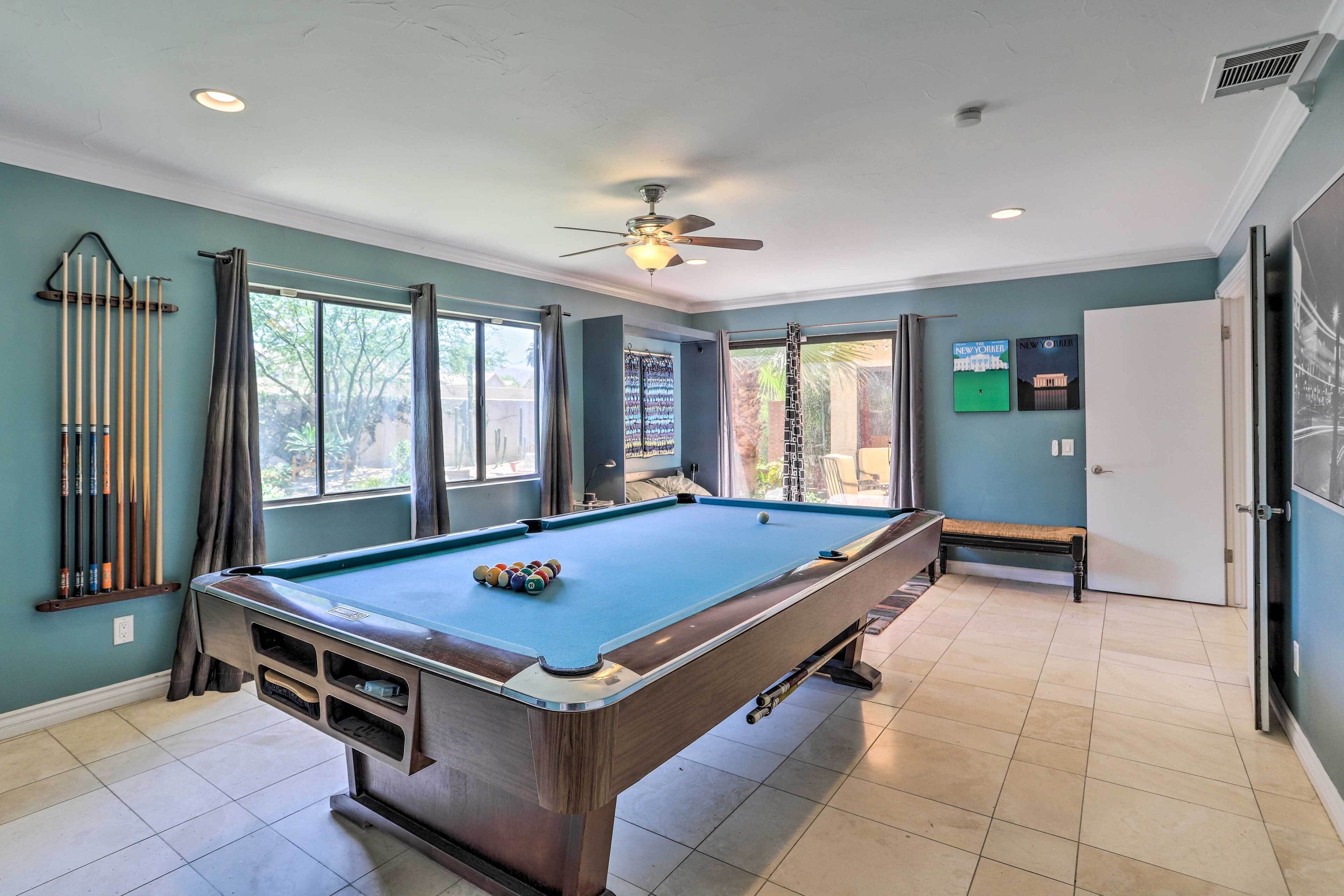 A pool table in a room with teal walls, a ceiling fan, and a window with curtains.