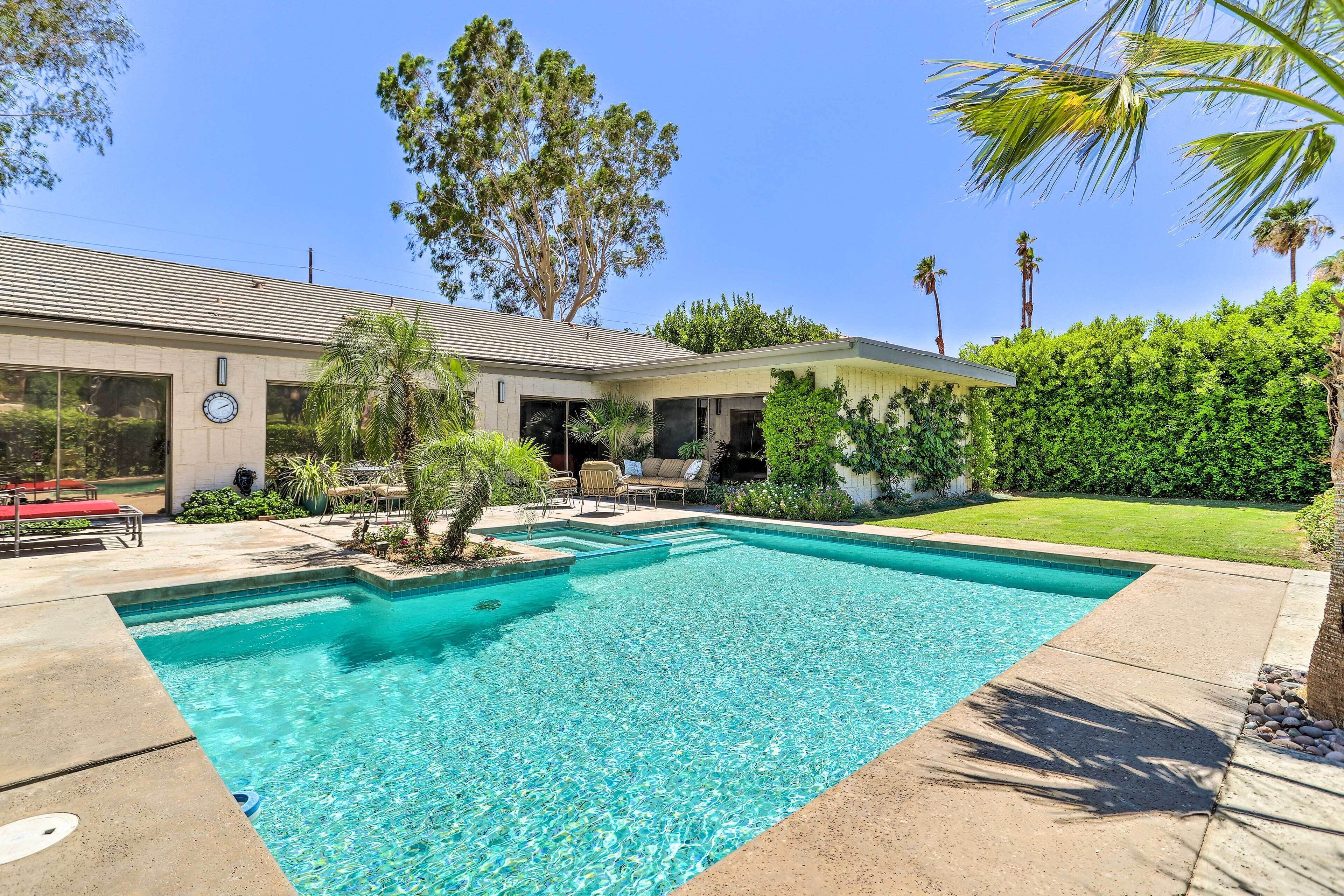 A swimming pool with a clear blue water, surrounded by a patio area with lounge chairs and a covered seating area.