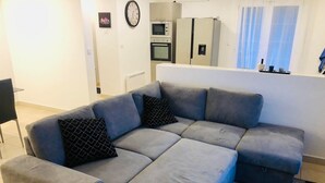 Un soggiorno moderno con un divano angolare grigio, un tavolino e un'area cucina sullo sfondo.