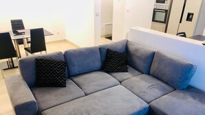 Un soggiorno moderno con un divano angolare grigio, un tavolo da pranzo con sedie e un angolo cottura dotato di elettrodomestici.