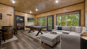 A wooden-paneled room with a pool table, a sofa, and a large window offering a view of greenery. - Private Location Hot tub, Pool table, Multicade, Free Attraction Passes (Sevierville)