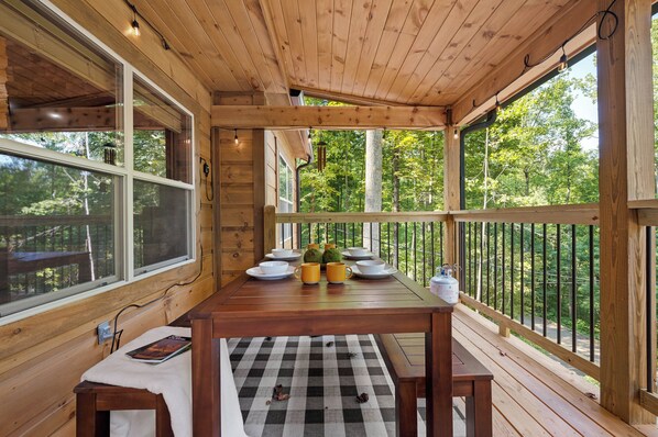 A wooden deck with a table set for dining, surrounded by large windows offering a view of the forest. - Private Location Hot tub, Pool table, Multicade, Free Attraction Passes (Sevierville)