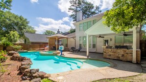 A backyard with a swimming pool, a covered patio, and a stone fireplace.