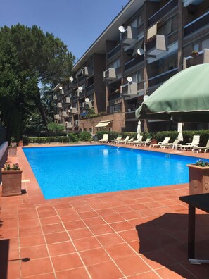 A swimming pool with sun loungers and a green umbrella, surrounded by a multi-story building with balconies and satellite dishes. - Aurelia Antica Suites & Apartments (Rome)