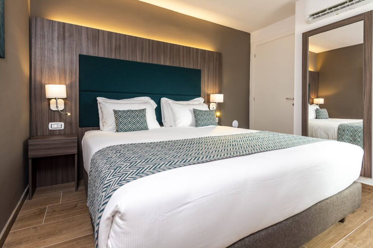 Een hotelkamer met een groot bed, twee nachtkastjes met lampen, een houten hoofdbord en een spiegel aan de muur.
