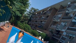 A swimming pool with two inflatable swan floats, surrounded by a multi-story building with balconies and satellite dishes.