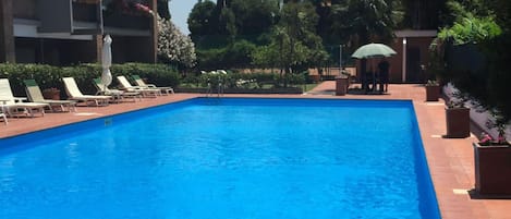 Una piscina rectangular con borde de azulejos, rodeada de sillones de descanso y plantas en macetas.