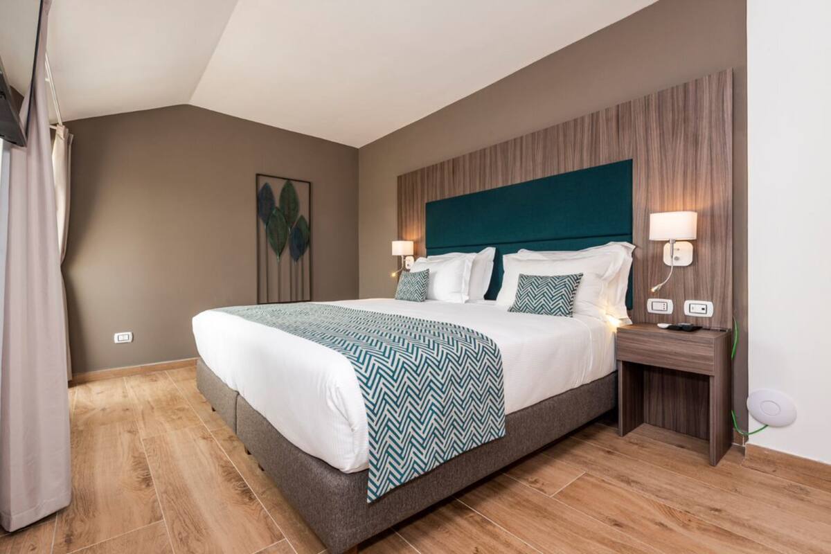 Een hotelkamer met een groot bed, een houten hoofdbord, twee bedlampen en een nachtkastje met een lamp.