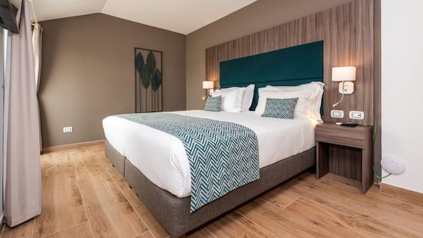 A hotel room with a large bed, a wooden headboard, two bedside lamps, and a nightstand with a lamp.