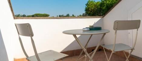 A small outdoor balcony with two metal chairs and a round table.
