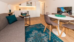A modern living room with a sofa, a dining table with chairs, a kitchen area, and a television.