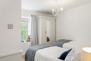 Quarto com duas camas, um guarda-roupa, janela com cortinas e um ursinho no peitoril.