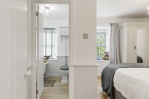 Quarto com uma cama, janela com cortinas, vista para o exterior e um urso de pelúcia no parapeito.