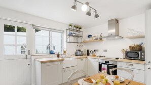 A modern kitchen with white cabinetry, a wooden countertop, and a dining area with a table set for breakfast. - Perfect for a Cornish getaway, Jade cottage is a charming cosy cottage. (St Agnes)