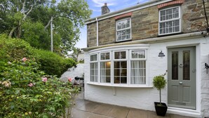 A two-story house with a white exterior, a curved bay window, and a door with a glass panel. - Perfect for a Cornish getaway, Jade cottage is a charming cosy cottage. (St Agnes)