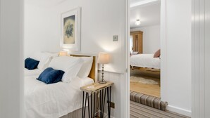 A hotel room with a bed, a bedside lamp, a painting on the wall, and a mirror reflecting another room. - Perfect for a Cornish getaway, Jade cottage is a charming cosy cottage. (St Agnes)