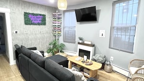 Un salon moderne avec un canapé d’angle noir, une table basse en bois et un téléviseur fixé au mur.