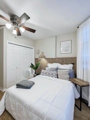 A bedroom with a bed, a ceiling fan, a bedside table, a radiator, and a door. - Cozy Oasis Mins to NYC Private Backyard Fireplace Grill  Firepit (Jersey City)