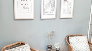 Une pièce comprenant deux fauteuils en osier, une petite table ronde et trois œuvres d’art encadrées accrochées au mur.