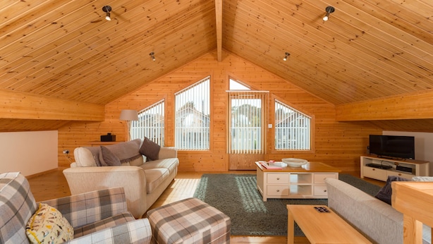 Un acogedor loft con techo de madera alto, un sofá, un reposapiés escocés, una mesita y un televisor.