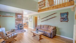 Un salon spacieux doté d’une cheminée, d’un escalier en bois et d’un canapé agrémenté de coussins à motifs.