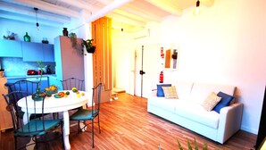 Ein modernes Wohnzimmer mit einem weißen Sofa, einem Esstisch mit Stühlen und einer Küche im Hintergrund.
