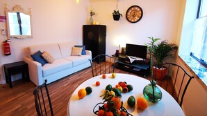 Ein Wohnzimmer mit einem weißen Sofa, einer schwarzen Unterhaltungseinheit, einem runden Tisch mit Obst und einem großen Fenster.