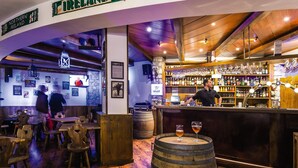 Una zona de bar con mobiliario de madera, un barman y una variedad de botellas y vasos en estanterías.