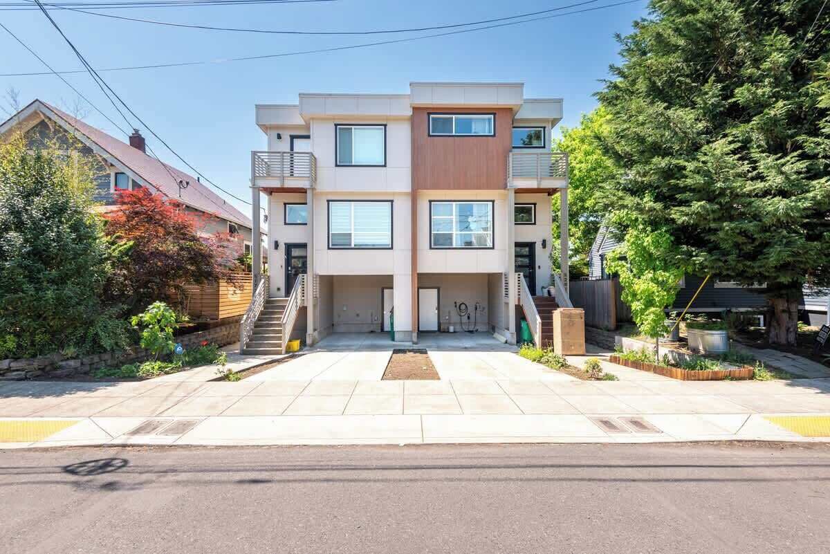 Un moderno edificio residenziale a più piani con un ingresso centrale, un'area parcheggio coperta e un giardino anteriore curato.