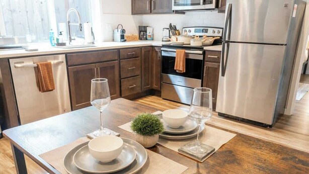 A modern kitchen with wooden cabinets, stainless steel appliances, and a dining table set with plates, bowls, and glasses. - Walkable Apt Next to Restaurants, Bars, and Shops! (Portland)