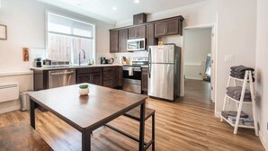 A modern kitchen with dark cabinets, stainless steel appliances, and a wooden dining table. - Walkable Apt Next to Restaurants, Bars, and Shops! (Portland)