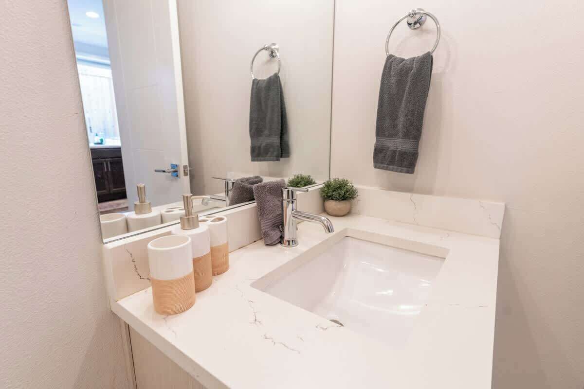 Une salle de bain avec un lavabo blanc, un miroir, deux serviettes, une plante en pot et des articles de toilette posés sur le comptoir.