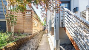 A narrow pathway flanked by wooden fences and a stone wall, leading to a building with a metal gate. - Walkable Apt Next to Restaurants, Bars, and Shops! (Portland)