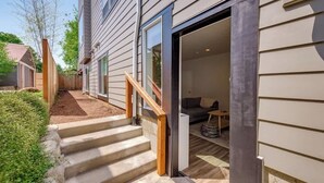 A residential exterior with a wooden staircase leading to a front door, a small porch area, and a visible living room with a sofa and coffee table. - Walkable Apt Next to Restaurants, Bars, and Shops! (Portland)