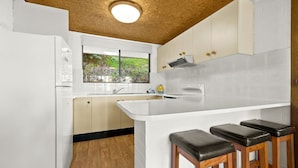 A modern kitchen with white cabinets, a wooden ceiling, and a window overlooking greenery. - Over The Boardwalk - North Narooma (North Narooma)