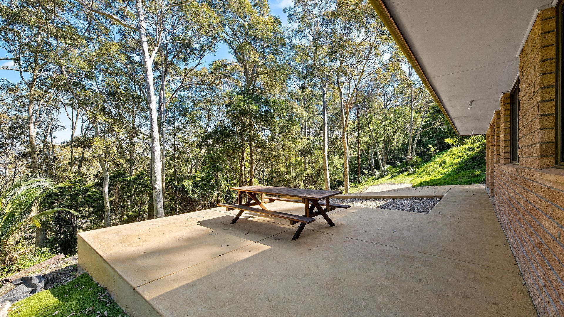 A picnic table on a concrete patio with a view of a forested hillside.