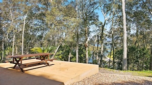 A picnic table in a forested area with a clear view of the surrounding trees and a body of water in the background. - Over The Boardwalk - North Narooma (North Narooma)