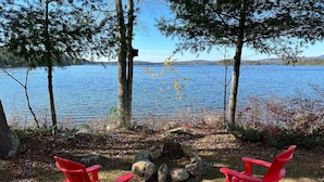 Deux chaises Adirondack rouges sont placées face à un lac, offrant une vue dégagée sur l’eau et les collines lointaines.