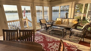 Une véranda dotée d’une grande fenêtre donnant sur un lac, aménagée avec une table à manger, des chaises et un canapé.